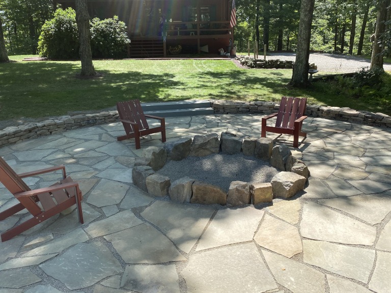 A fire pit surrounded by lawn chairs on a rock hardscaping installation